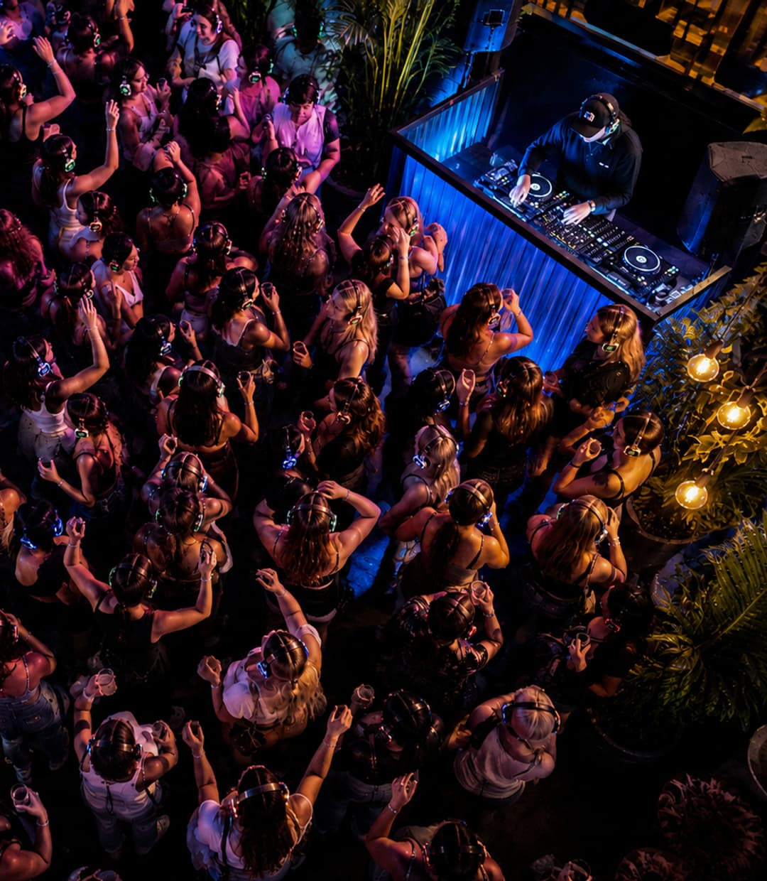 Dansvloer van bovenaf, tientallen oplichtende koptelefoons voor de verlichte dj-booth