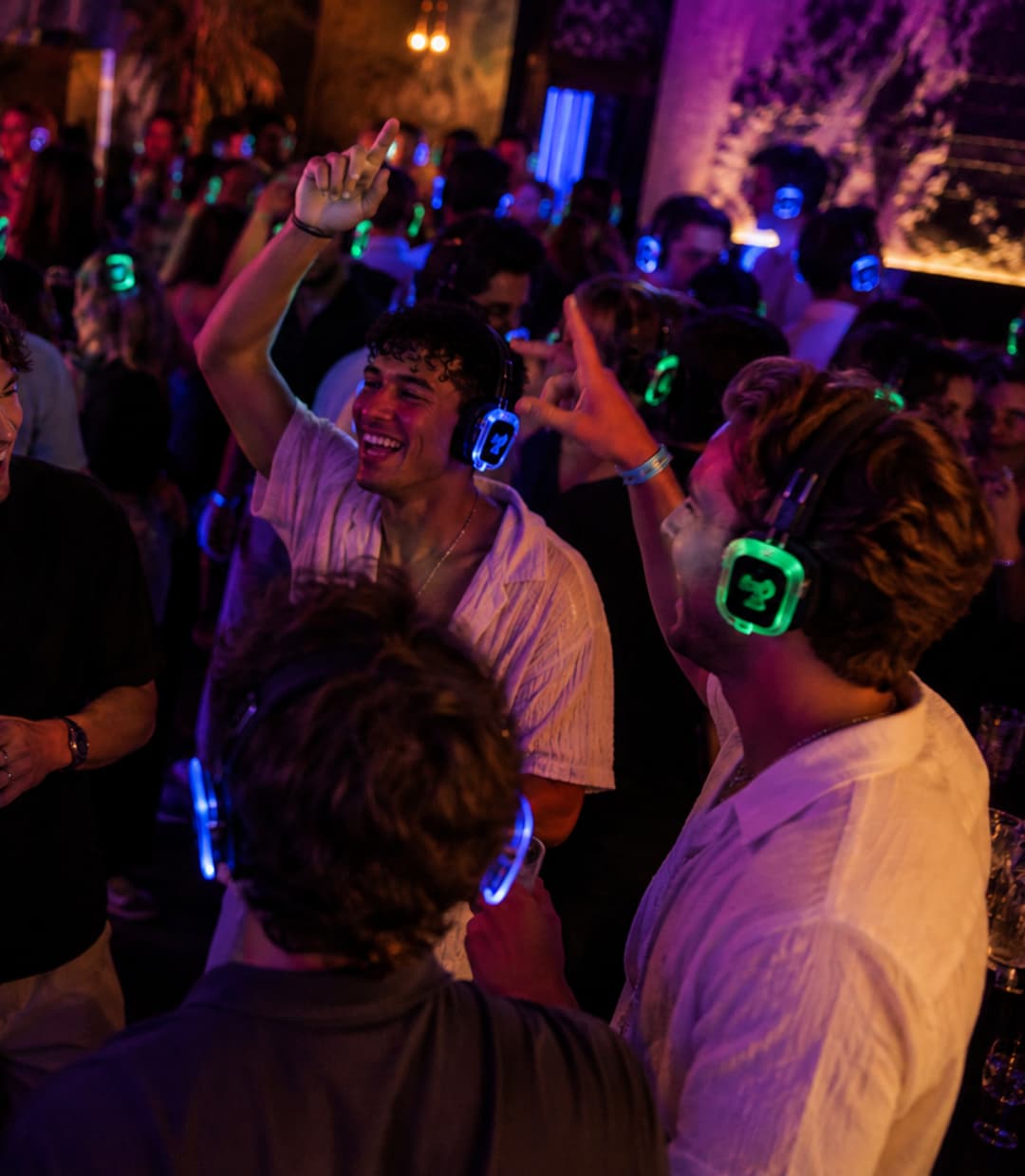 Vrienden dansen en zingen door elkaar heen met blauw en groen verlichte koptelefoons op